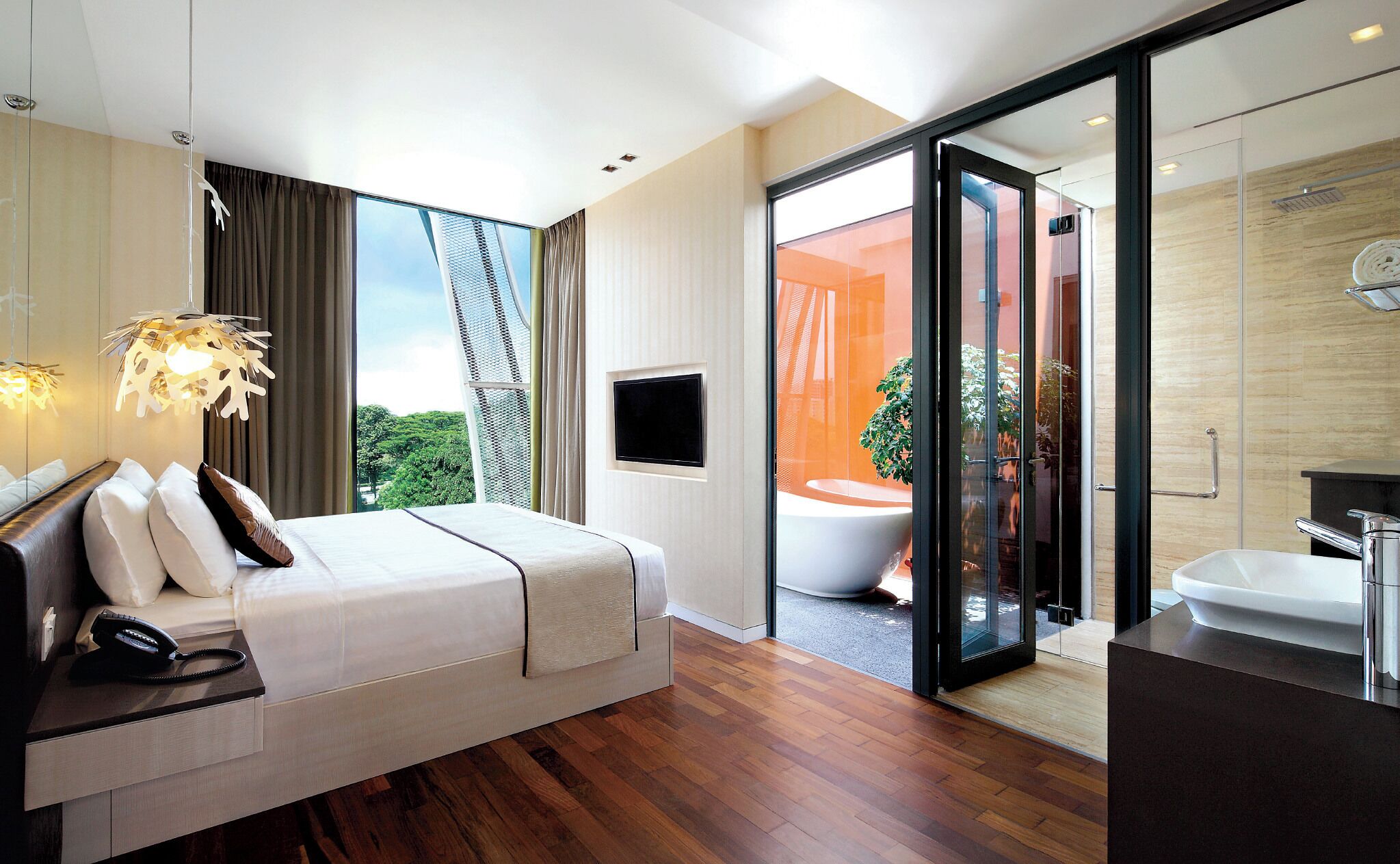 A modern hotel room with a bed, a TV, a bathroom with a bathtub, and a view of greenery outside.