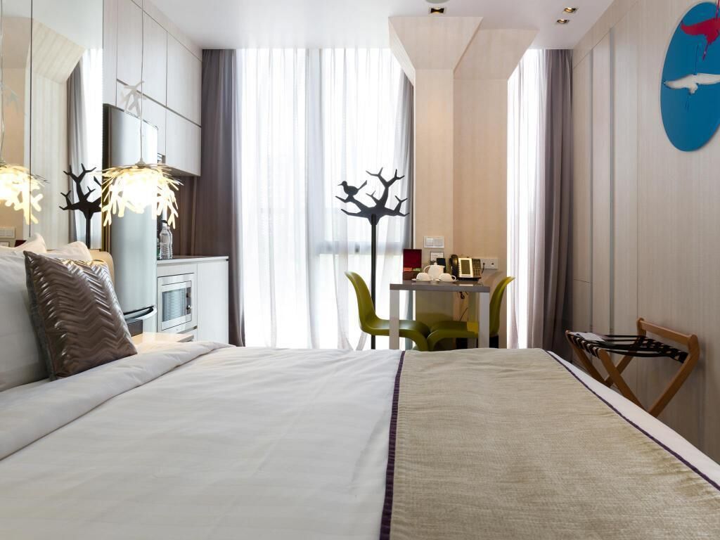 A hotel room with a bed, a desk, a chair, a lamp, and a wall-mounted artwork.