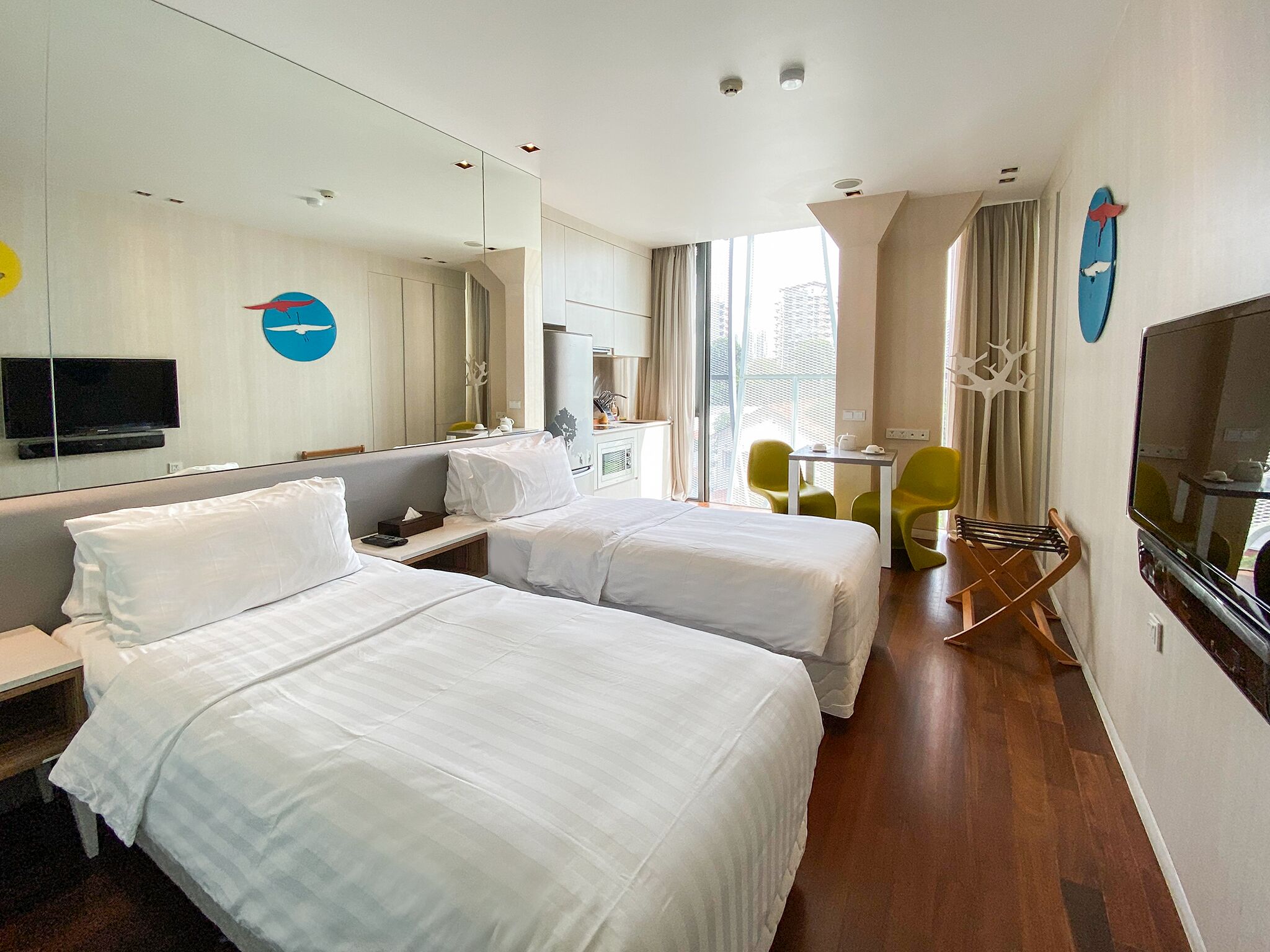 A hotel room with two beds, a desk, a chair, a TV, and a large window.