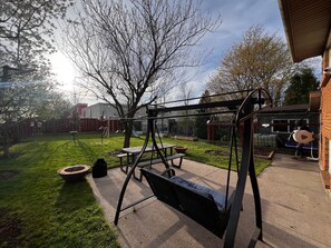 Ein Garten mit Schaukel, Picknicktisch und Gartenschlauch.