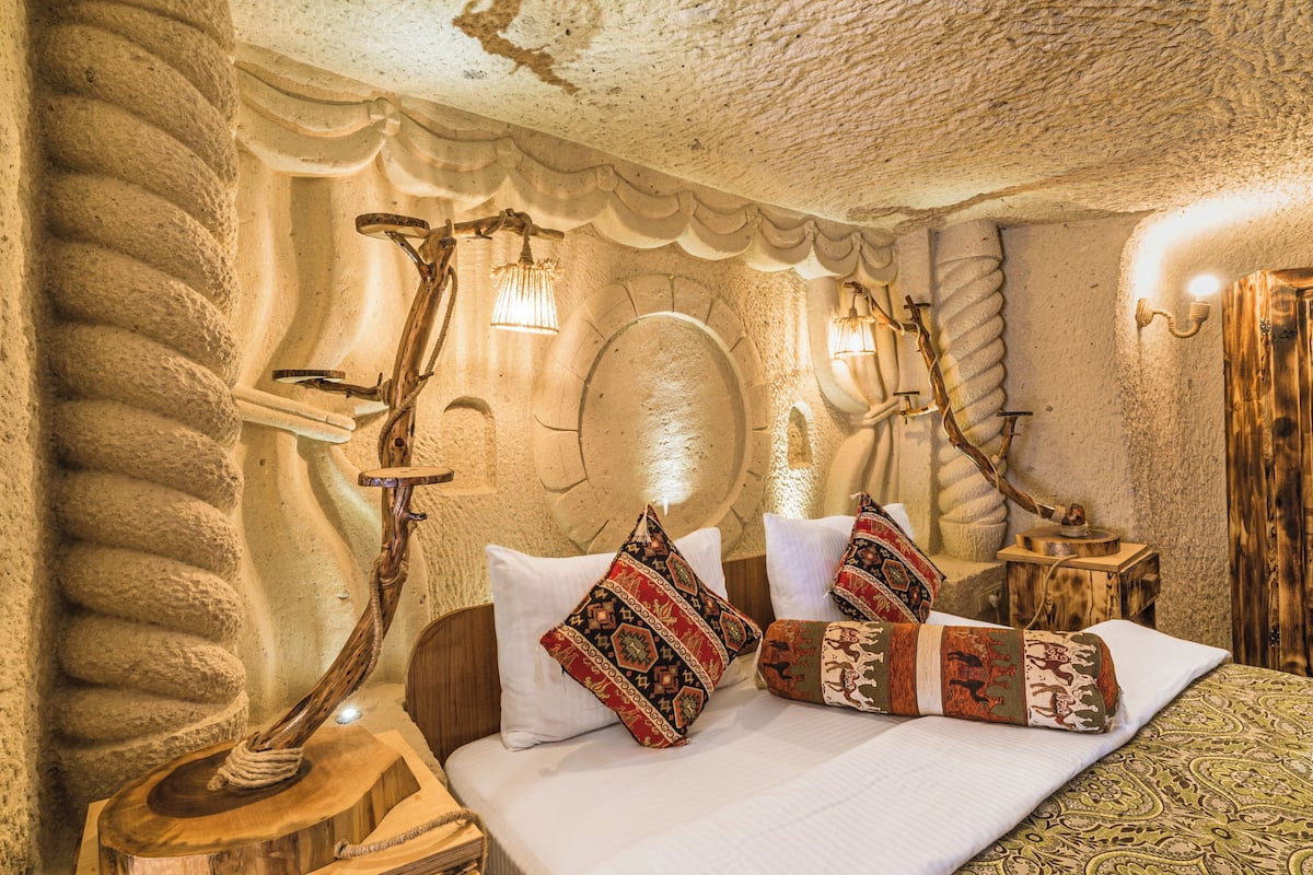 Ein Zimmer mit einer Steinwand, einem hölzernen Bett mit gemusterten Kissen und einer einzigartigen Holzlampe.