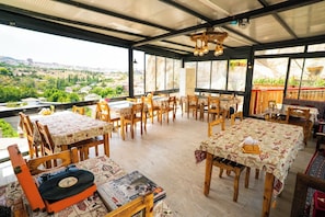 A restaurant with outdoor seating, wooden tables, and chairs, and a view of a cityscape. - Cappadocia Ennar Cave and Swimming Pool (Nevşehir)