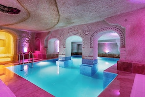 An indoor swimming pool with clear blue water, stone walls, and decorative arches. - Cappadocia Ennar Cave and Swimming Pool (Nevşehir)