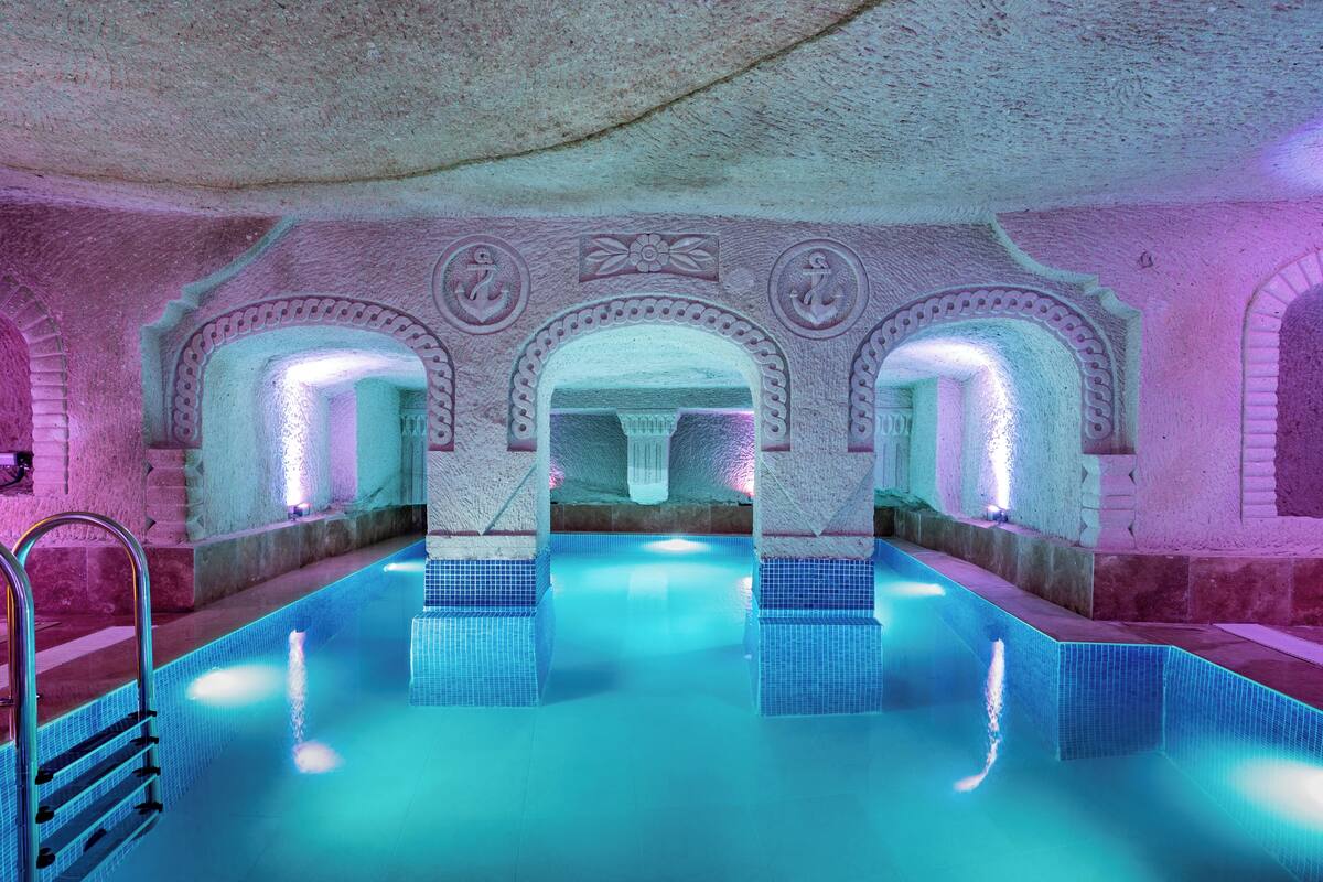 Ein Innenpool mit klarem Wasser, umgeben von Steinmauern und Bögen, und eine Metallleiter, die zum Pool führt.