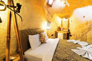 A room with a bed, a wooden headboard, a nightstand, a mirror, and a small table with a lamp. - Cappadocia Ennar Cave and Swimming Pool (Nevşehir)