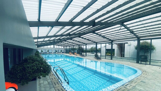 Ein Innenpool mit klarem, blauem Wasser, umgeben von Liegestühlen und einem überdachten Bereich mit Metallveranda.