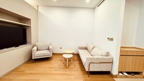 Ein modernes Wohnzimmer mit Flachbildfernseher, zwei Sofas, einem kleinen runden Tisch und einer Holzkabine.