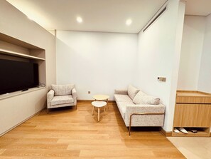 A modern living room with a flat-screen TV, two sofas, a small round table, and a wooden cabinet. - Lancaster Luminaire - Hoba Housing (Hà Nội)