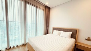 Ein Hotelzimmer mit einem großen Bett, einem Holzkopfteil, einem Nachttisch und Blick durch transparente Vorhänge.