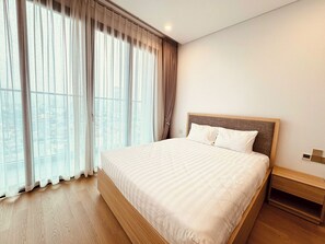 A hotel room with a large bed, wooden headboard, a nightstand, and a view through sheer curtains. - Lancaster Luminaire - Hoba Housing (Hà Nội)