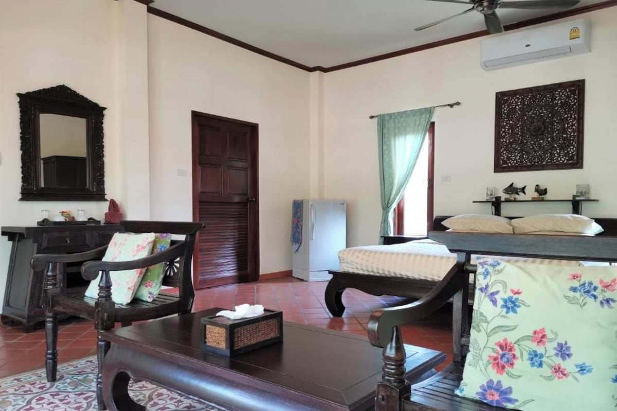 A room with a wooden bench, a small table with a tissue box, a mirror, a door, a window with curtains, and a ceiling fan.