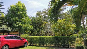 A red car parked in a well-maintained garden with hedges and trees. - Tuna Resort by Zuzu (Rawai)