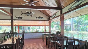 A covered dining area with tiled flooring, wooden tables and chairs, ceiling fans, and fish wall art.