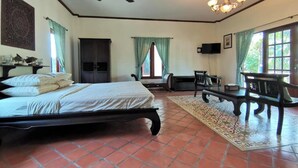 A bedroom with a bed, a ceiling fan, a TV, a desk, and a window with curtains.
