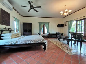 A bedroom with a bed, a ceiling fan, a TV, a desk, and a window with curtains.