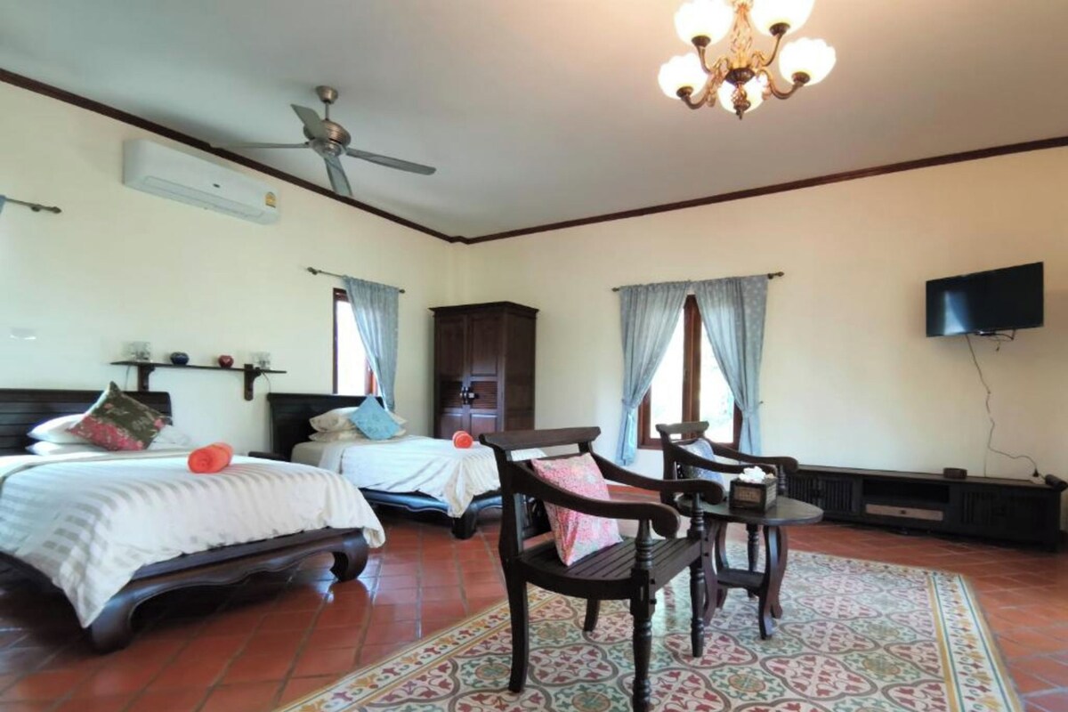 A hotel room with two beds, a ceiling fan, a chandelier, a television, and a patterned rug.