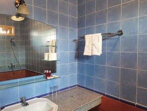 A bathroom with blue tiles, a glass shower enclosure, a sink, and a towel rack.