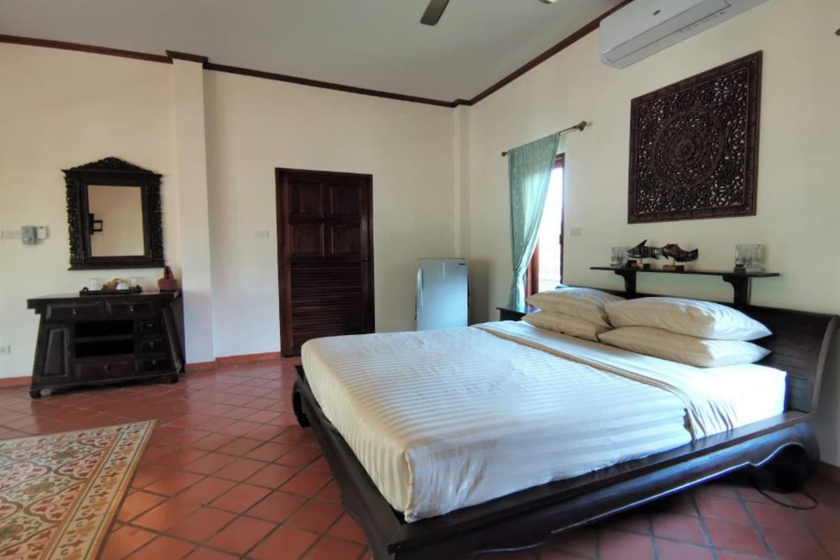 A bedroom with a bed, a ceiling fan, a dresser, a mirror, a door, and a wall-mounted air conditioner.