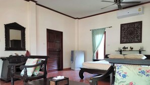 A room with a wooden bench, a small table with a tissue box, a mirror, a door, a window with curtains, and a ceiling fan. - Tuna Resort by Zuzu (Rawai)