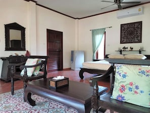 Quarto com um banco de madeira, uma mesa pequena com uma caixa de lenços, um espelho, uma porta, uma janela com cortinas e um ventilador de teto.