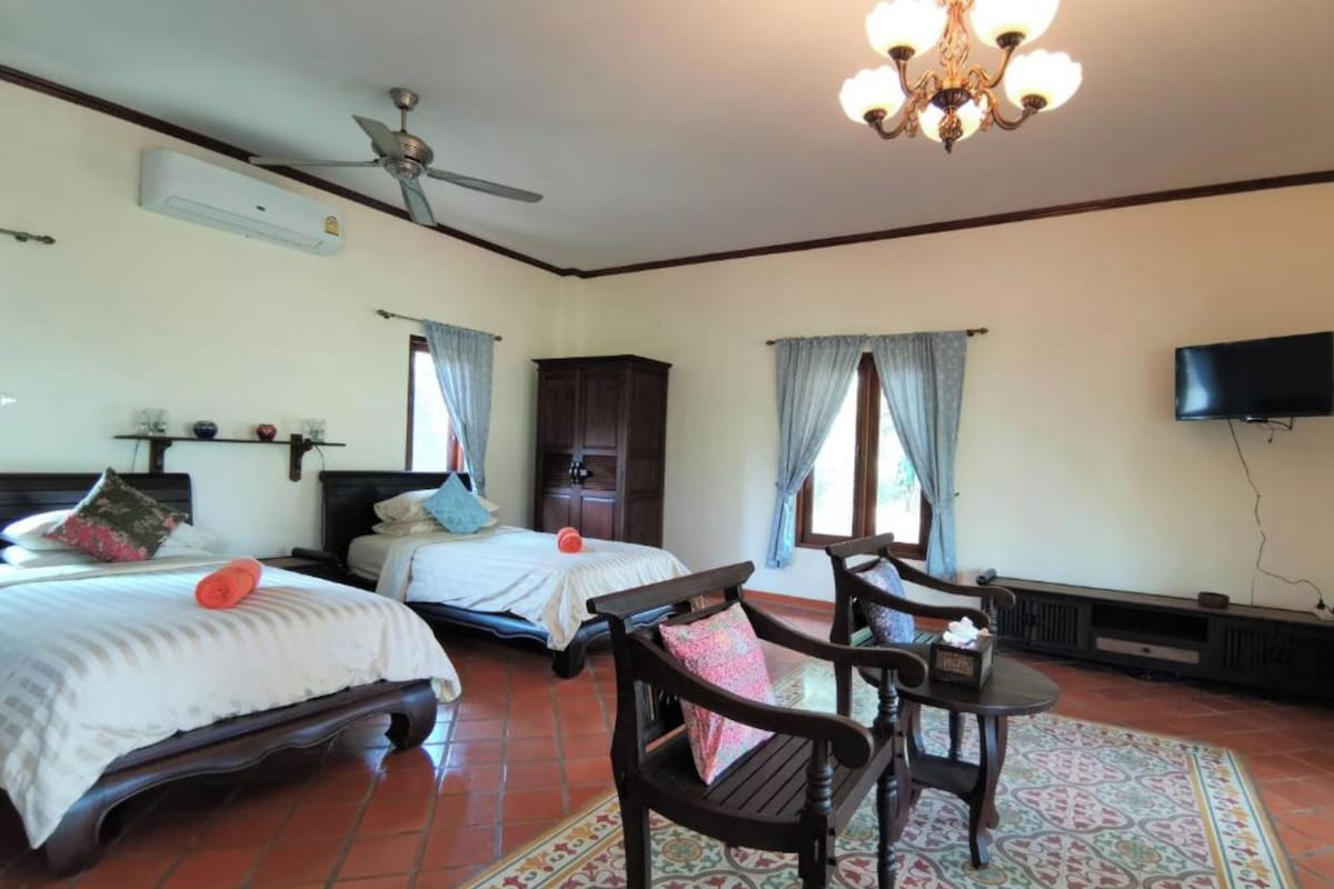 A hotel room with two beds, a ceiling fan, a TV, and a wooden cabinet.