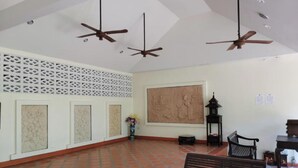 A spacious room with a tiled floor, a large wall-mounted painting, ceiling fans, and a bench. - Tuna Resort by Zuzu (Rawai)