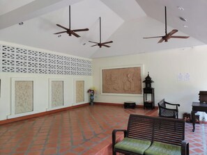 Um quarto amplo com piso de azulejos, uma pintura grande pendurada na parede, ventiladores de teto e um banco.