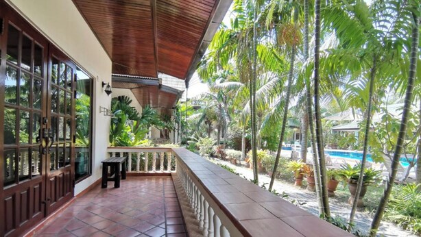 A covered outdoor area with a tiled floor, a wooden railing, and a view of a pool and palm trees. - Tuna Resort by Zuzu (Rawai)