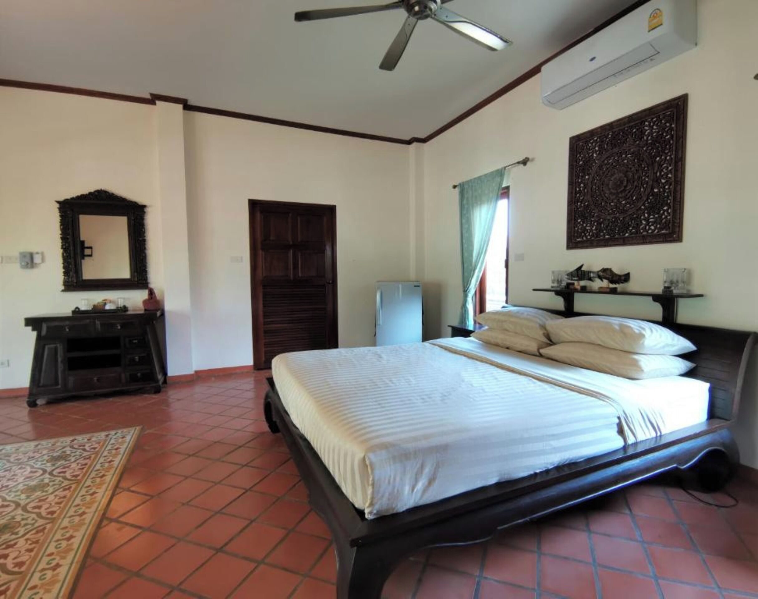 Une chambre à coucher comprenant un lit, un ventilateur de plafond, une commode, un miroir, une porte et un climatiseur fixé au mur.