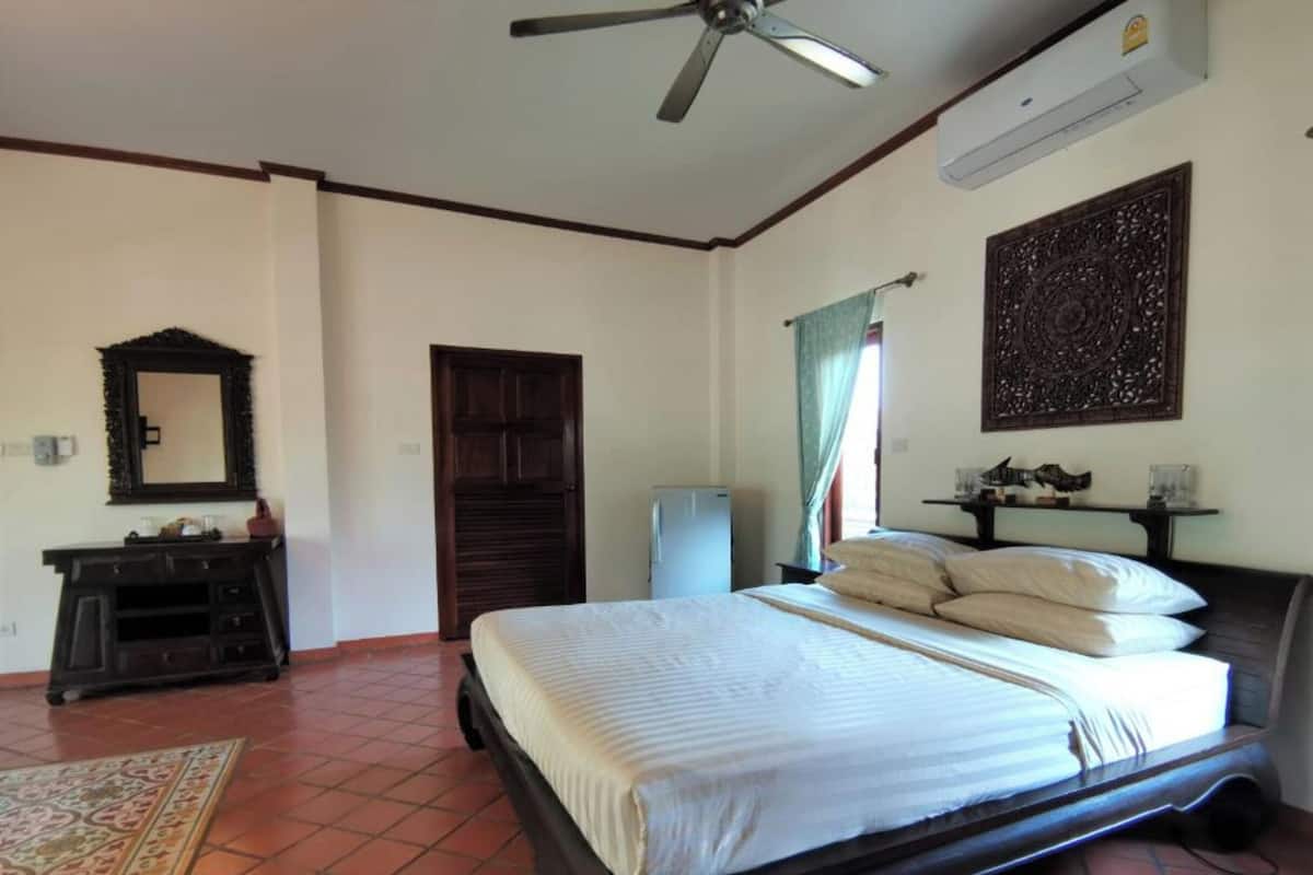 Une chambre à coucher comprenant un lit, un ventilateur de plafond, une commode, un miroir, une porte et un climatiseur fixé au mur.