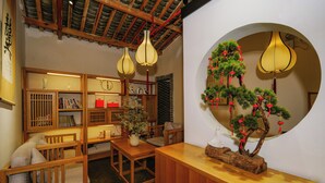 Una habitación tradicional japonesa con suelo de tatami, mobiliario de madera, un bonsái y un espejo redondo.