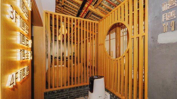 Una habitación con un separador de madera, un ventanal circular y un electrodoméstico blanco en el suelo.