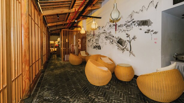 A corridor with wooden paneling, woven seating, and a mural on the wall. - Gongxili - Yujian Hotel (Kunming)