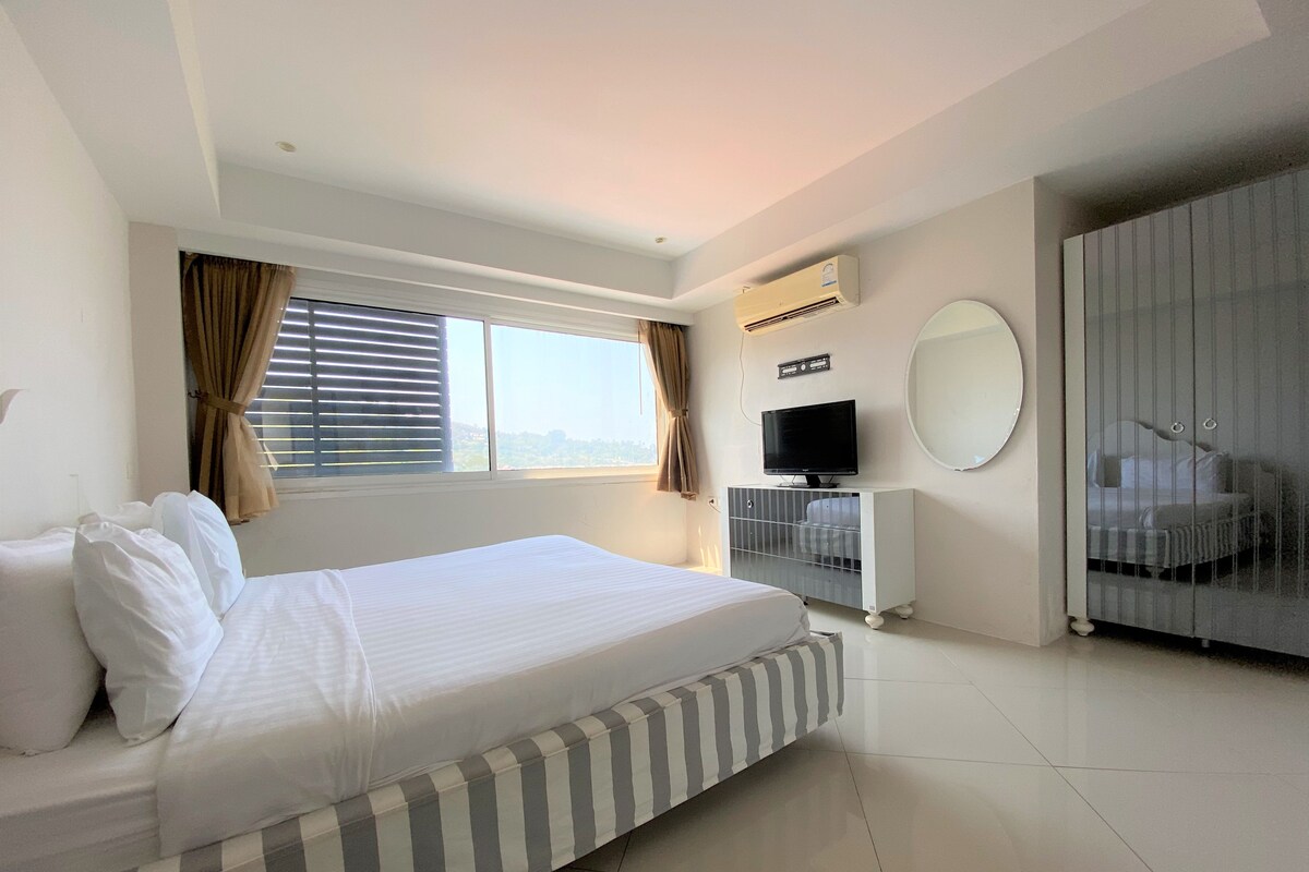A hotel room with a bed, a television, a wardrobe, and a window with curtains.