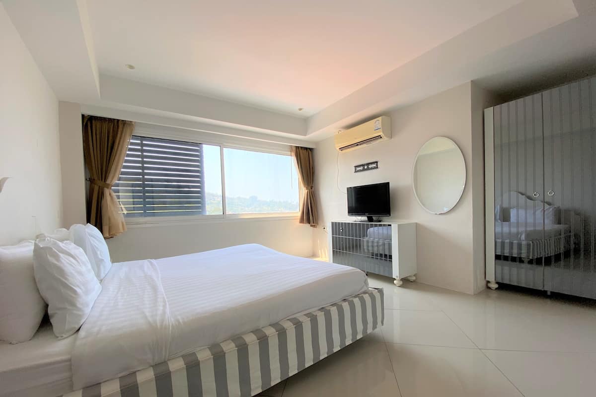 A hotel room with a bed, a television, a wardrobe, and a window with curtains.