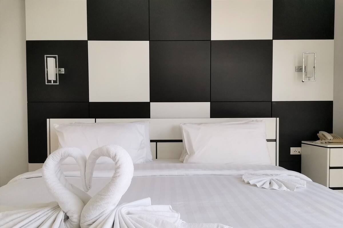 A hotel room with a checkered black and white headboard, a neatly made bed with white linens, and a telephone on the bedside table.