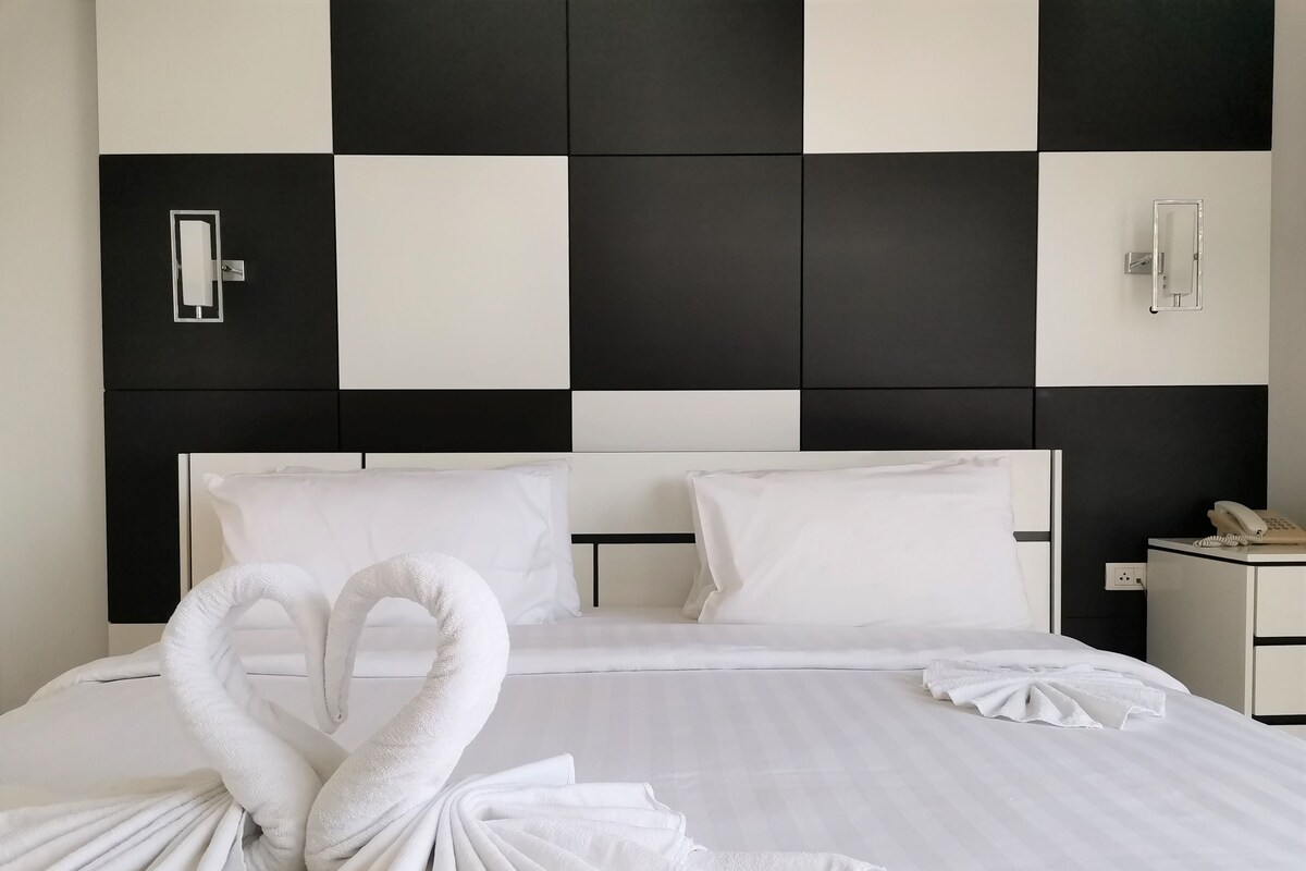 A hotel room with a checkered black and white headboard, a neatly made bed with white linens, and a telephone on the bedside table.