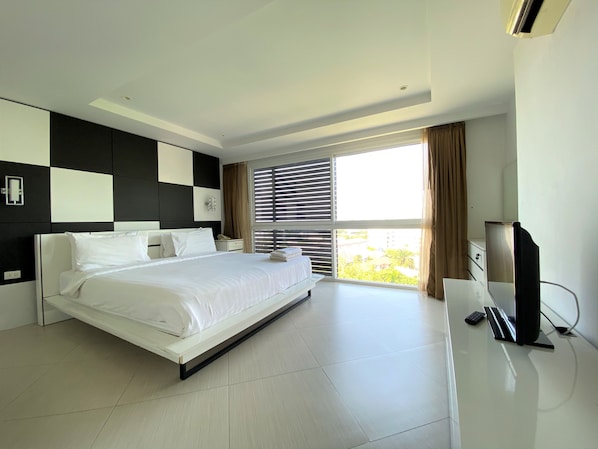 Une chambre d’hôtel moderne dotée d’un grand lit, d’un téléviseur à écran plat et offrant une vue sur la verdure environnante.