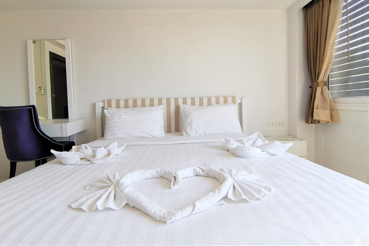 A hotel room with a bed, a chair, a bedside table, a mirror, and a window with curtains.
