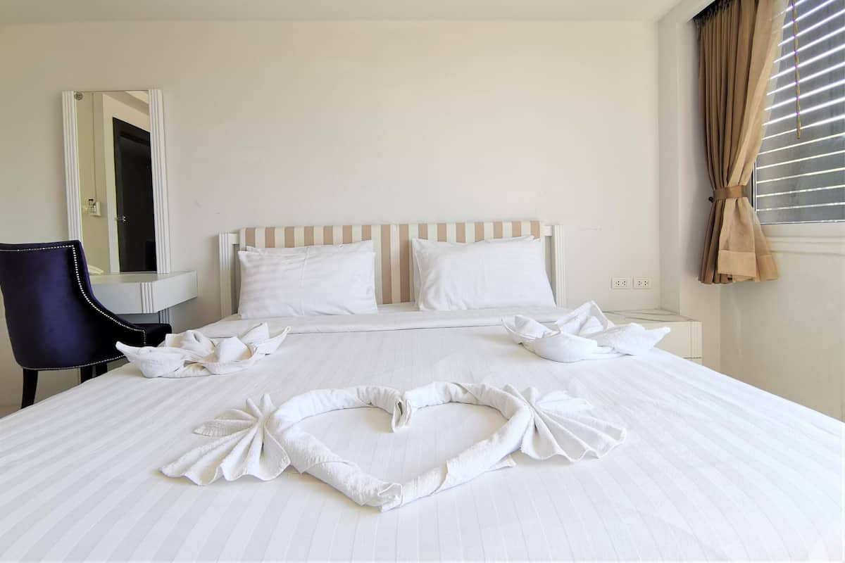 A hotel room with a bed, a chair, a bedside table, a mirror, and a window with curtains.
