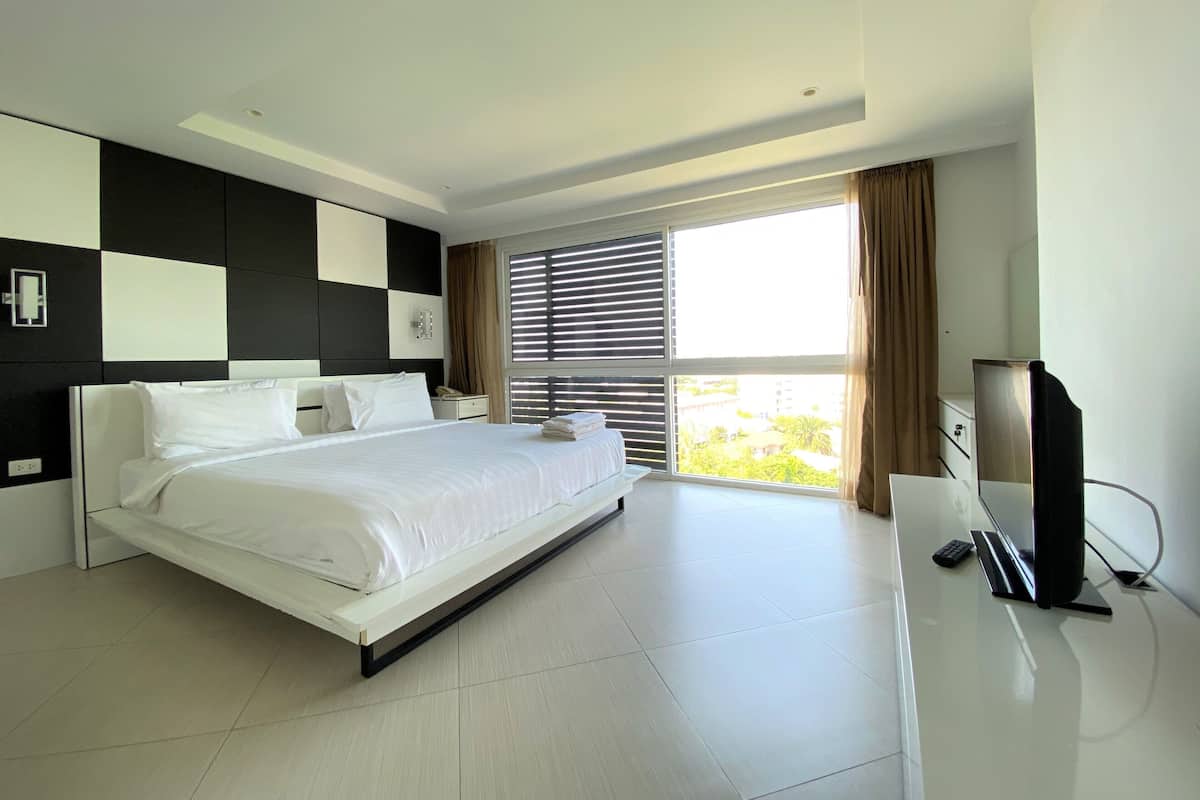 A modern hotel room with a large bed, a flat-screen TV, and a view of greenery outside.