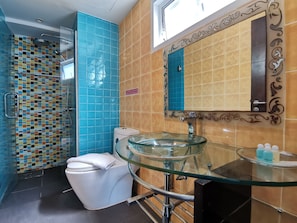 Une salle de bain avec un lavabo en verre, des toilettes blanches et un espace douche aux carreaux bleus.
