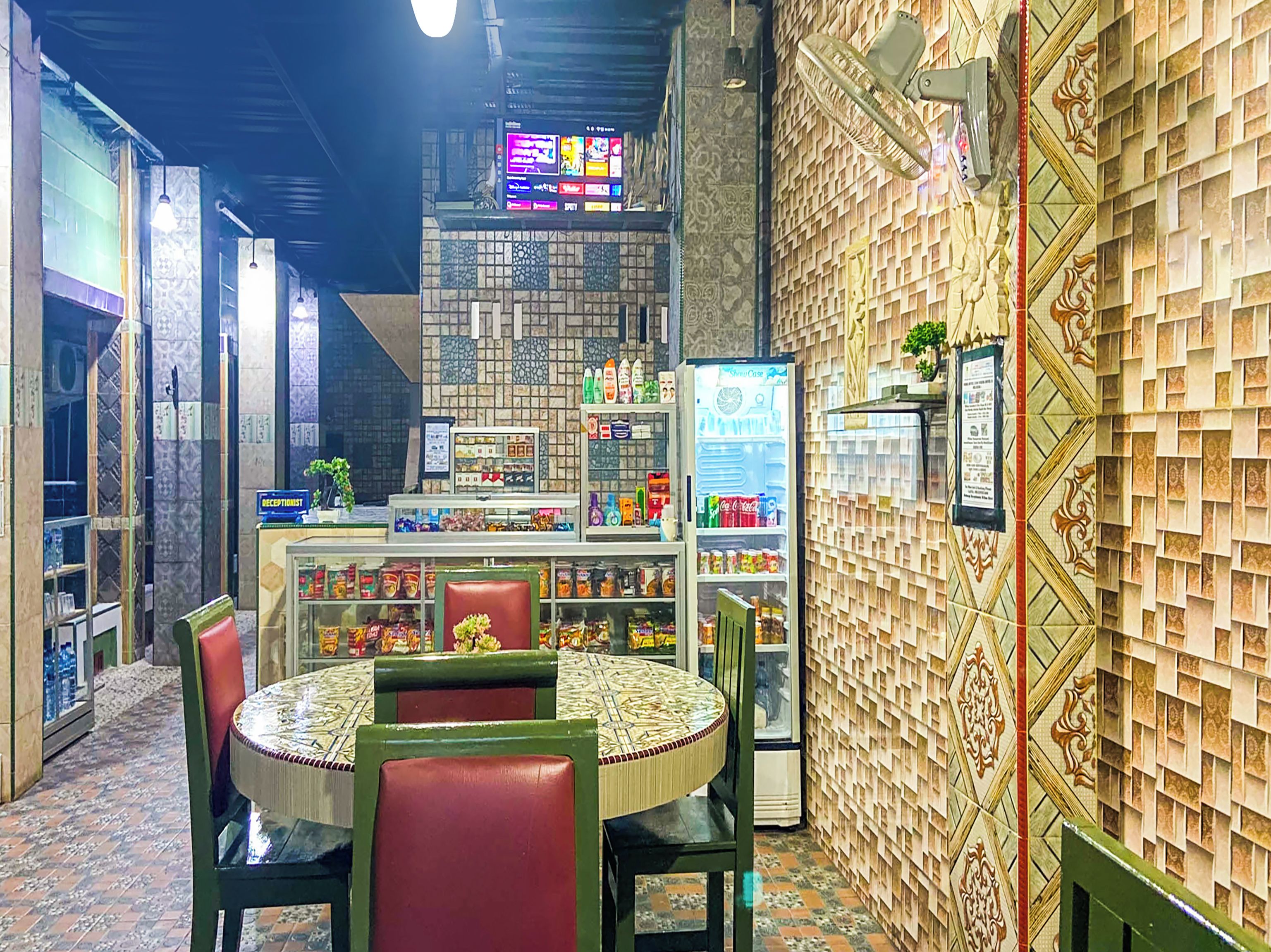 A restaurant interior with a round table, chairs, a counter with a beverage cooler, and a patterned wall.