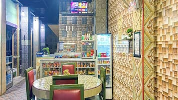 A restaurant interior with a round table, chairs, a counter with a beverage cooler, and a patterned wall.