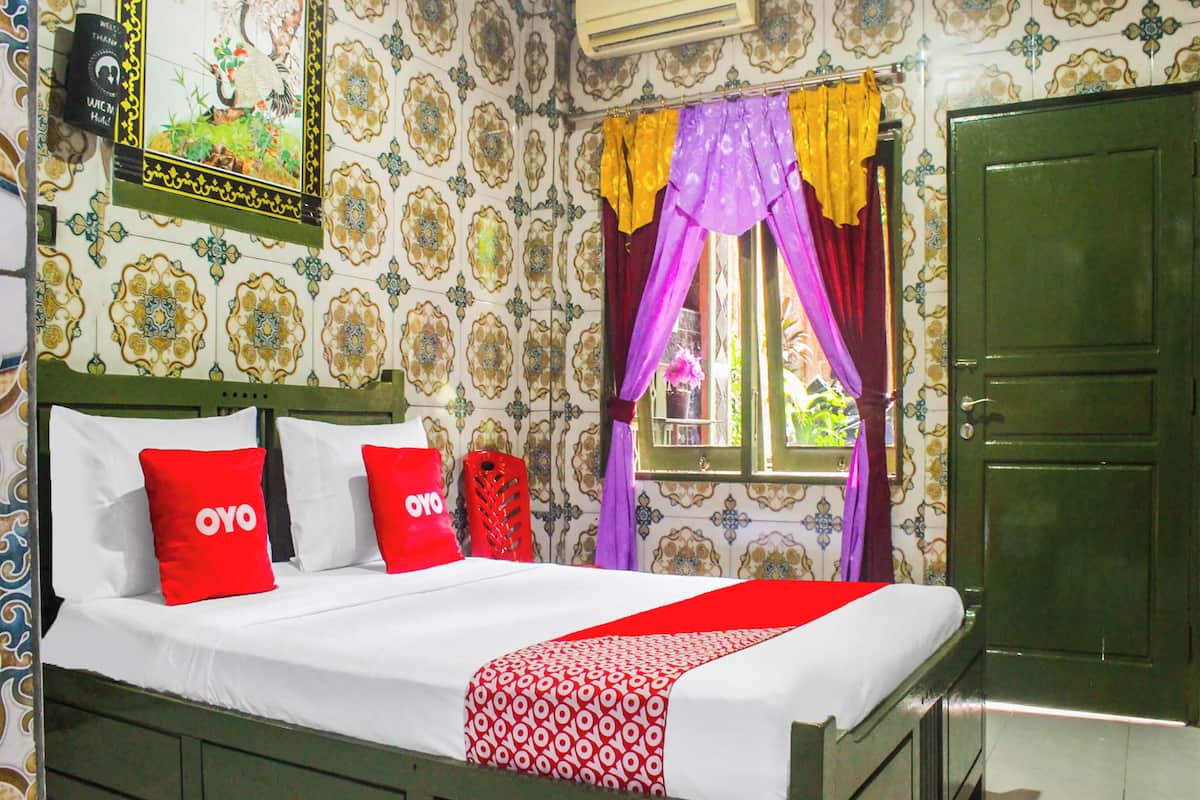 A bed with white bedding and red pillows, a green door, and patterned wallpaper.