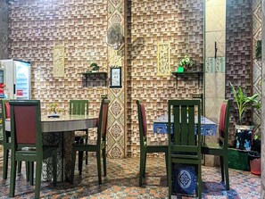 Un comedor con pared decorada, sillas verdes, una mesa y un refrigerador.