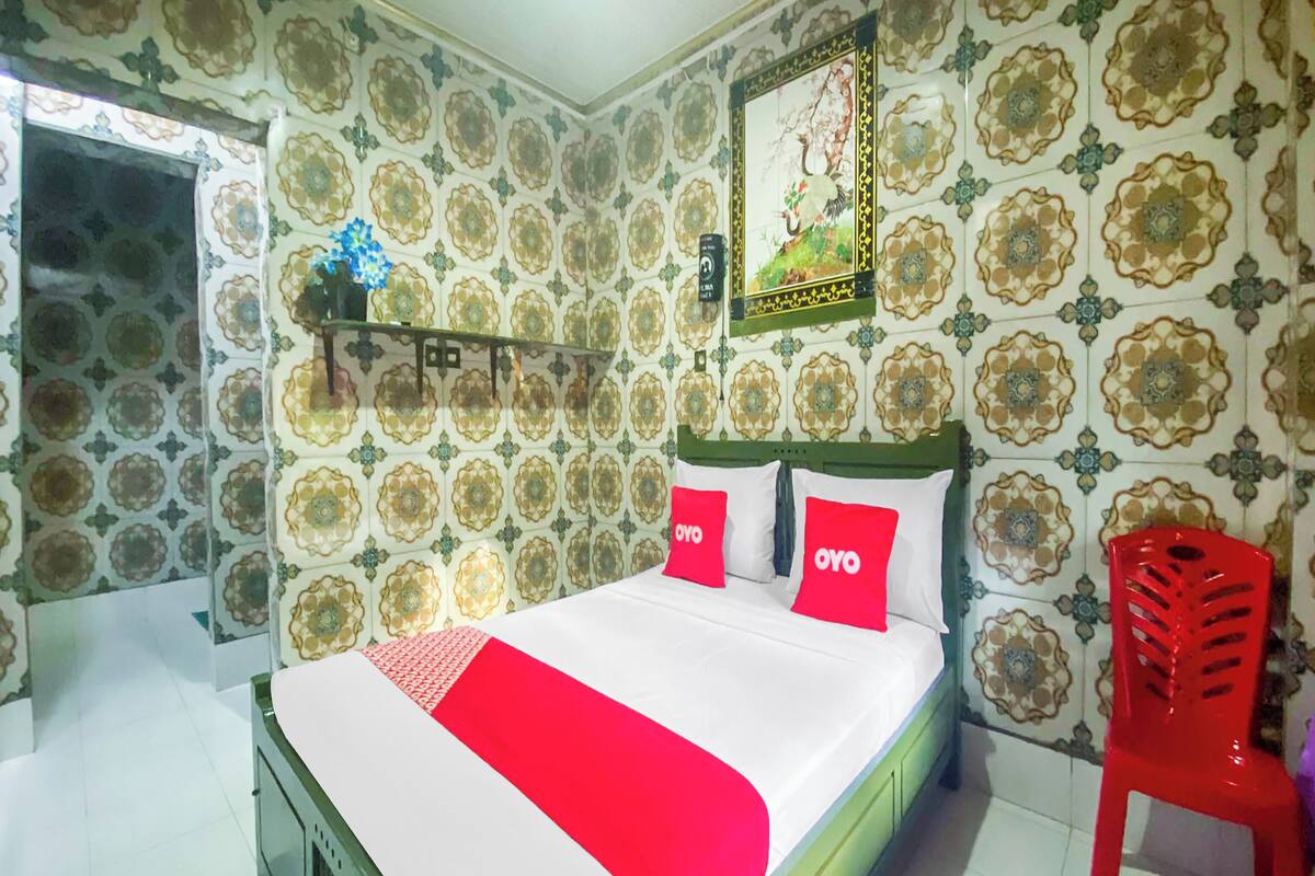 A bedroom with a bed, a red chair, and patterned wallpaper.