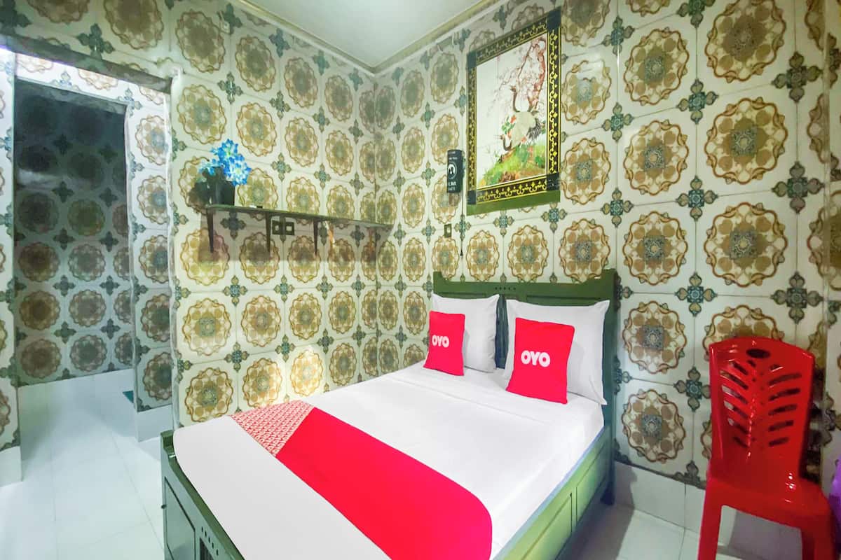 A bedroom with a bed, a red chair, and patterned wallpaper.