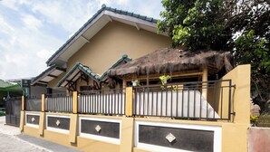 A house with a thatched roof, a gated entrance, and a paved driveway. - Oyo 2392 Kost Safira (Ngaglik)