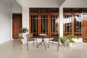 Une pièce avec une porte en bois, une fenêtre avec des cadres en bois, une table ronde avec deux chaises et des plantes en pot.